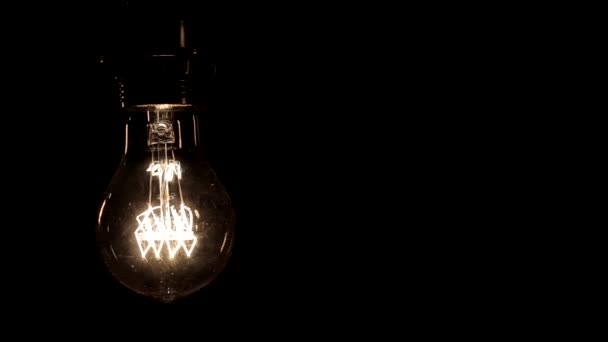 暖かい光が黒の背景に軽く揺れるエジソンランプのクローズアップ — ストック動画