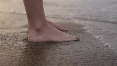 İnsan ayakları kumda duruyor ve deniz dalgalarıyla yıkanıyor.