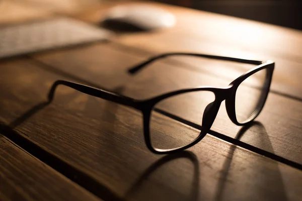 木製のテーブルの上のコンピュータからの視力と視力の補正と保護のためのメガネ — ストック写真