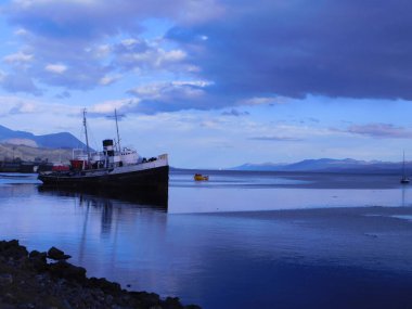 Güzel bir gökyüzünün altında terk edilmiş bir gemi ve gün batımında mavi bir su.