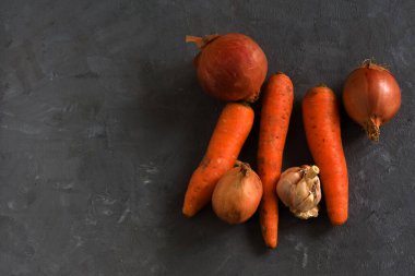 Gri bir masada havuç, soğan ve sarımsak..