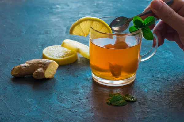 Bir el kaşıkla, bir fincan zencefilli çay ve limon kırsal mavi bir masada..