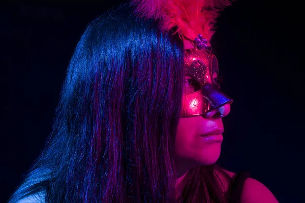 A woman in a red mask in a bar with pink and blue light.