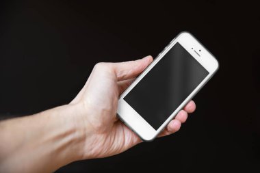Siyah arkaplanda boş ekranlı akıllı telefon tutan adam. Telefonlu erkek eller, metin için boşluk
