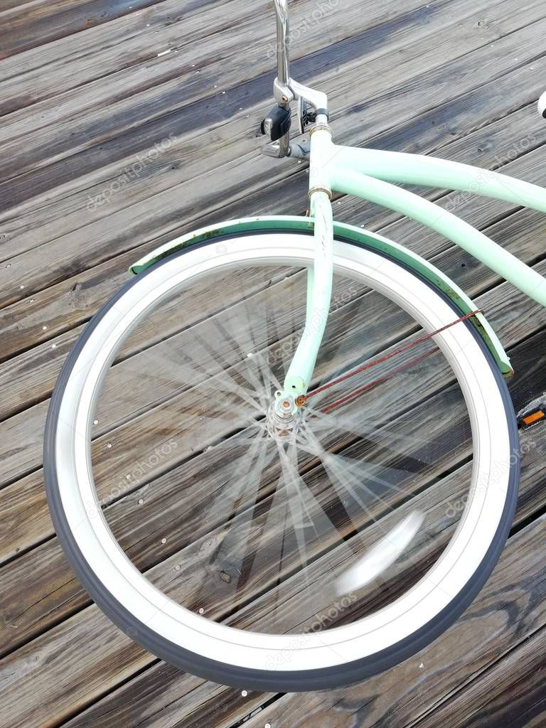 white wheel of old turquoise bicycle rotates on wooden surface