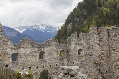 Çok iyi korunmuş taş kale, yeşilliklerle çevrili bir dağda, uzak mesafeden karlı dağları görebilirsin, bulutlu gökyüzünü.