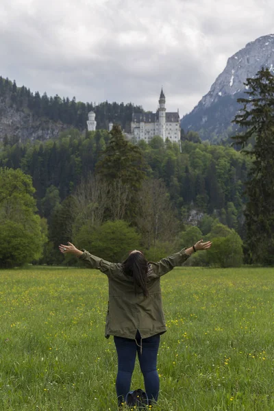 Neuschwanstein şatosunda fotoğraf çekimi, etkileyici Alman şatosuyla manzara, arka planda şatoyla poz veren insanlar, yeşil çayır, bol bitki örtüsü.