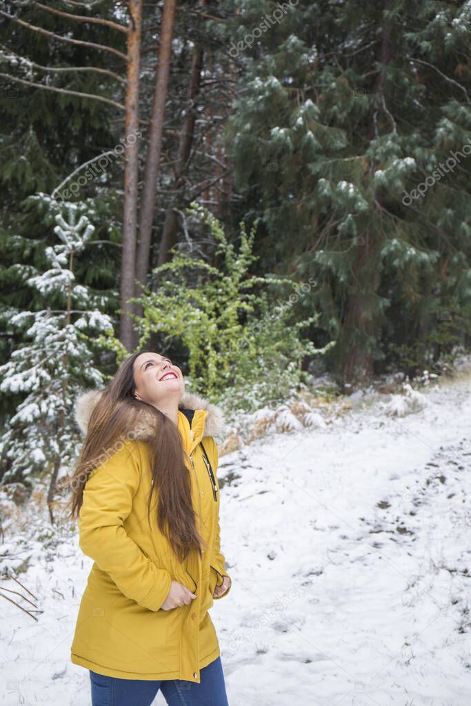 brunette woman with loose hair and yellow coat happy on a snowy day in the field