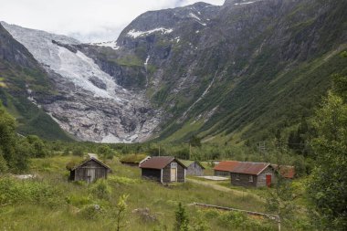 Terk edilmiş köy, farklı renkte ahşap evler, dağların arasında, arka planda buzullar, Norveç 'te bir yaz gününde bol miktarda yeşil bitki örtüsü.