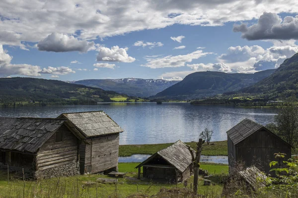 Kartpostal köyü, göl kıyısındaki cennet gibi ahşap köy, yaz mevsiminde Norveç, mavi gökyüzü biraz beyaz bulutlu, mavi su, yeşil çimen, ahşap evler