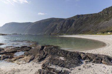 Renkli zıtlıklar, beyaz kumsal, ve kristal berrak mavi deniz, dağlar, yeşil çimenler, bazı kayalar ve açık mavi gökyüzü
