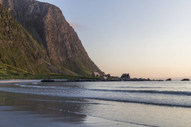 Sersemletici ve ıssız bir kumsalda gün batımı, kristal berrak su ve yeşil dağlar