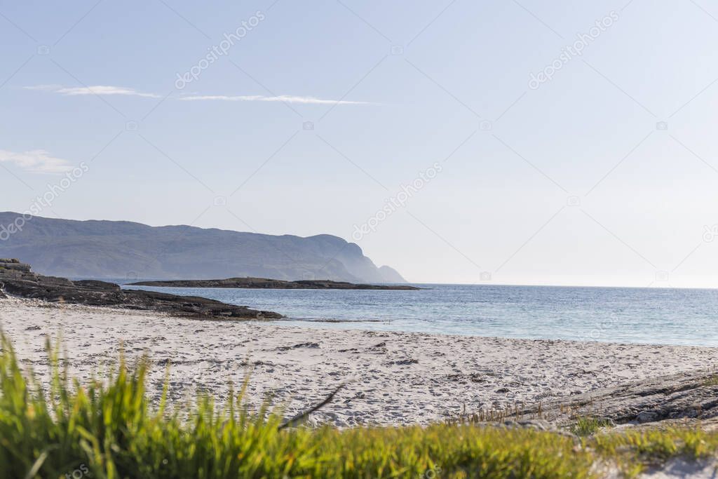  colorful contrasts, white sand beach, and crystal clear blue sea, mountains, green grass, some rocks and clear blue sky