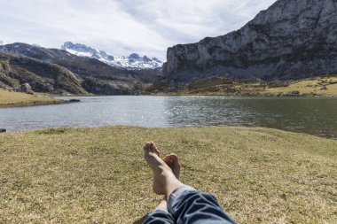 Çimlerin üzerinde çıplak ayak, arka planda bir göl ve Picos de Europa dağları.