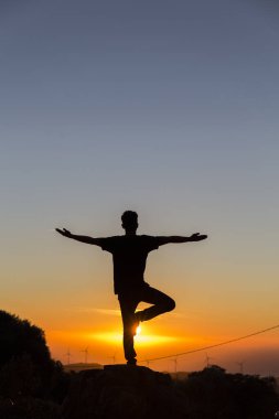 Açık bir günde gün batımını izlerken yoga yapan bir adamın arka ışığı