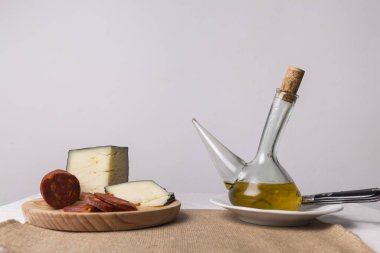 Peynir ve sucuklu ahşap bir tahtanın yanında zeytinyağlı cam kap.