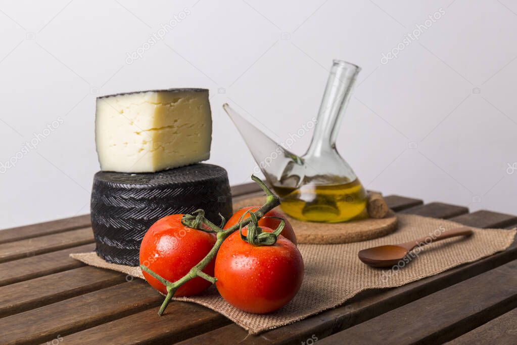 glass bowl with olive oil next to some red tomatoes and cheese on a wooden table