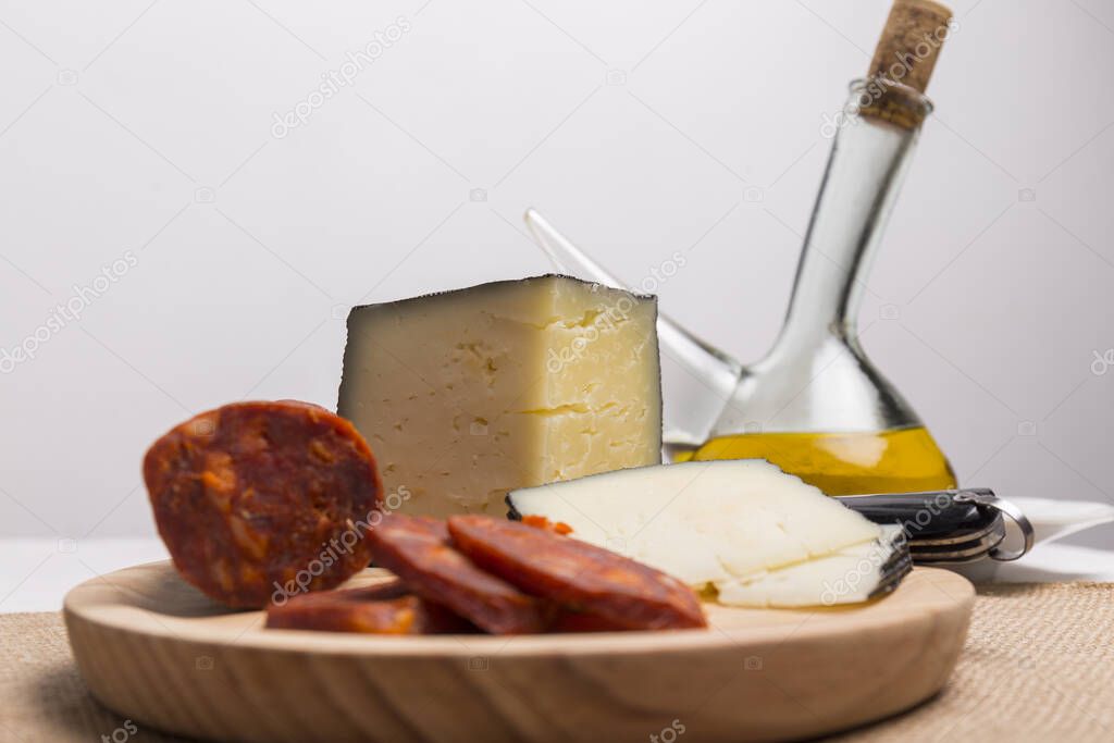 glass container with olive oil next to a wooden board with cheese and chorizo