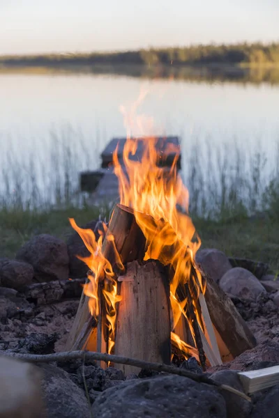 bonfire lit to the lake of a calm water lake during the sunset on a camping trip