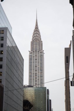New York 'taki Chrysler binası, diğer gökdelenlerin ortasındaki sokaktan bakıldığında gökyüzü gri.