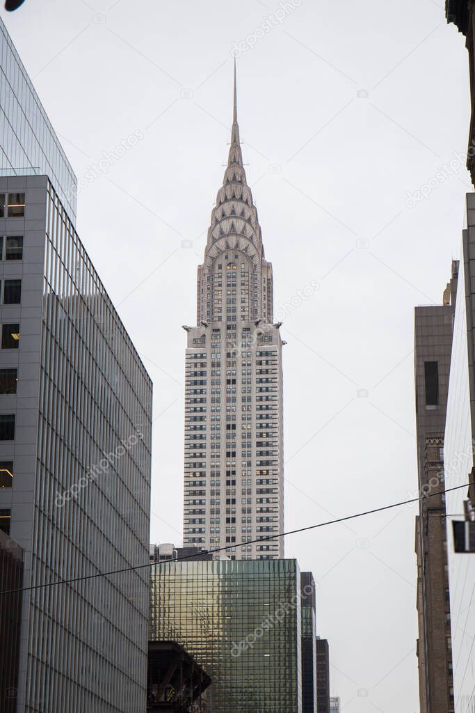 chrysler building in New York, seen from the street in the middle of other skyscrapers, the sky is gray