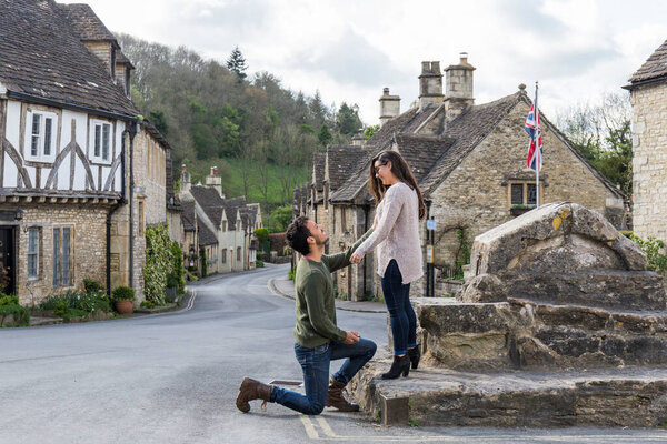 Petition for marriage, the man is kneeling asking the woman to marry in the square of a town in the south of England called Castle Combe