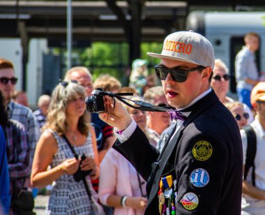 Lund, İsveç - 19 Mayıs 2018: Öğrenci üniforması, beyzbol şapkası ve güneş gözlüğü takmış bir adam Lundakarnevalen geçit törenine katılırken fotoğraf çekiyor
