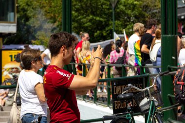Malmö, İsveç - 20 Temmuz 2019: Kırmızı tişörtlü, bronzlaşmış genç bir adam geçit törenine hayran kaldı ve İsveç 'in Malmö kentinde düzenlenen yıllık eşcinsel onur yürüyüşü sırasında cep telefonuyla fotoğrafını çekmeye başladı.