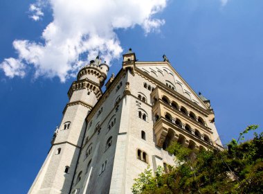 Hohenschwangau, Gemany - 20 Temmuz 2018: Sıcak bir yaz gününde açık mavi gökyüzüne yükselirken Neuschwanstein kalesinin ön cephesi ve kulesinin alçak açılı görüntüsü