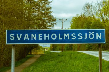 Snogeholmsjon adında bir göle ulaştığımızı gösteren bir trafik işareti. İşaret, uzaklardan esen bir kır yolunun yanına konur.