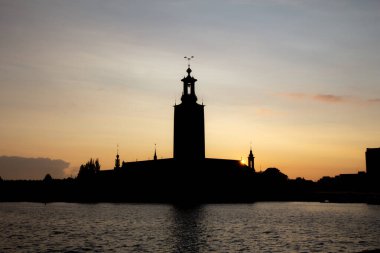 Stockholm Belediye Binası 'nın ikonik silueti arkasında güneş batarken Swedens başkentinde sıcak bir yaz akşamında.