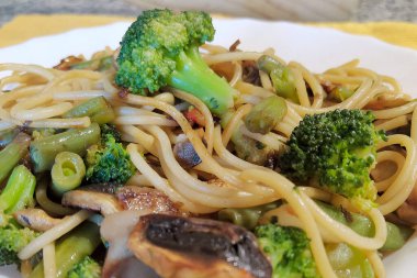 Vitamin ve mineraller açısından zengin bir Akdeniz diyeti için ekstra saf İspanyol zeytinyağıyla sotelenmiş taze sebzeli sağlıklı makarna tabağı.