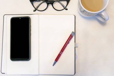 Smasrtphone, kahve fincanı, kalem ve gözlüklü beyaz ofis masası sağ tarafta tasarım metni eklemek için boşluk bırakıyor.