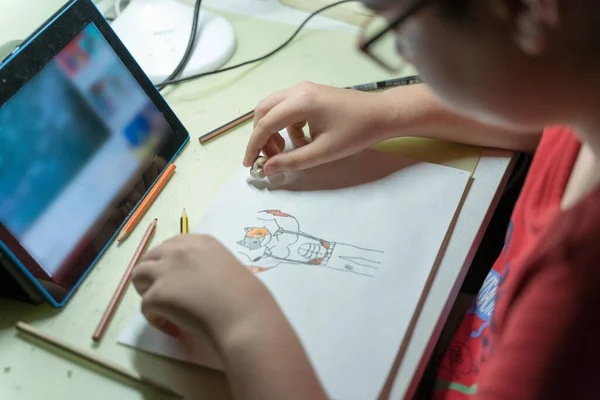 young person drawing a picture or comic book at home communicating online with a tablet for social distancing by covid-19 coronavirus