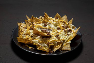 Koyu arkaplanda peynir ve sos olan nacho.