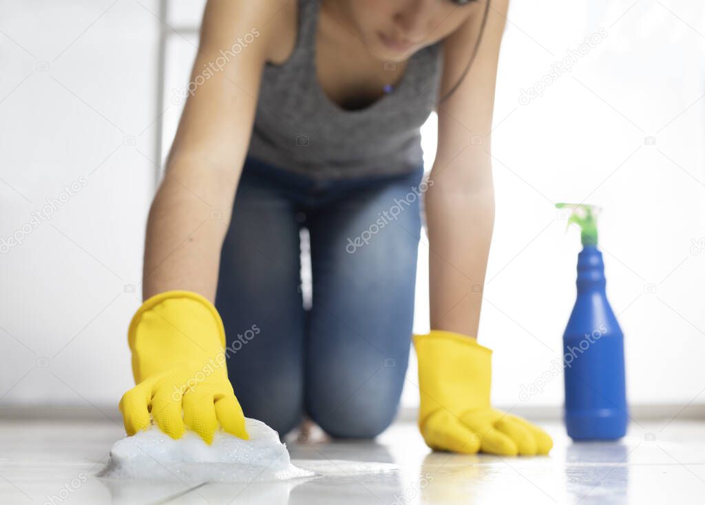 Woman on her knees disinfecting ceramic floor with gloves, sponge, spray, water and soap,gloves,knees,soap,foam,shiny,bright,latex,coronavirus,covid-19,pandeia,contagion