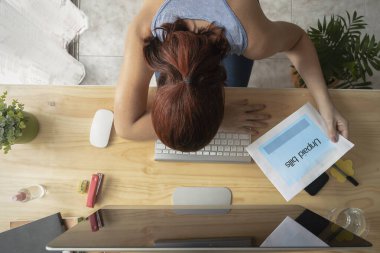 Kafasını bilgisayarın klavyesine yaslamış, elinde kağıt kağıtlarla faturaları ödeyen bir kadın..