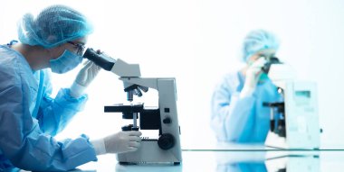 Biyogüvenlikli kadın doktorlar mikroskop altında virüs analizi yapıyorlar, salgın hastalık konsepti.