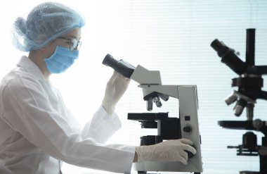 Kadın doktor ışık mikroskobu kullanarak koronavirüs üzerinde çalışıyor.
