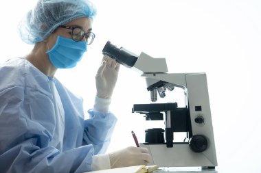 Biyolojik güvenlik giysisi içindeki kadın doktor gündemde virüs notları tutuyor.