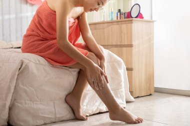 Havlulu kadın bacaklarına krem sürüyor.