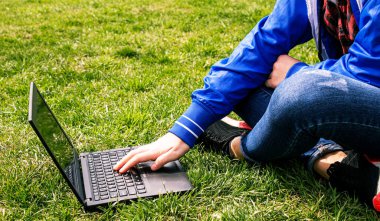 Çimlerin üzerinde dizüstü bilgisayarı olan bir kız. Mesafe dersi. İnternet dersleri. seçici odak