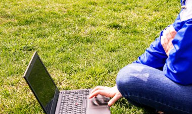 Çimlerin üzerinde dizüstü bilgisayarı olan bir kız. Mesafe dersi. İnternet dersleri. seçici odak