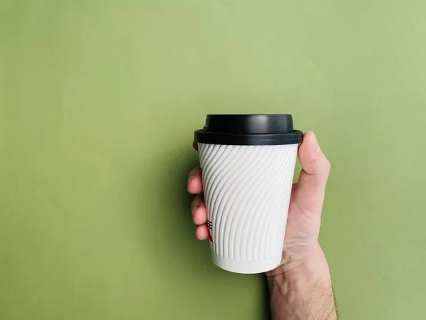 A man hand holding a paper cup with no label in front of colorful background with copy space.