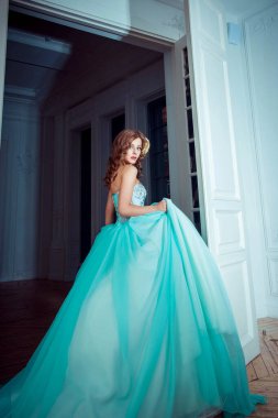 Güzel genç kız uzun, muhteşem turkuaz elbiseli prenses bir ışık kalesinde duruyor. Peri masalı moda fotoğraf çekimi Külkedisi. Güzel oda. Prenses kapıya doğru koşar.