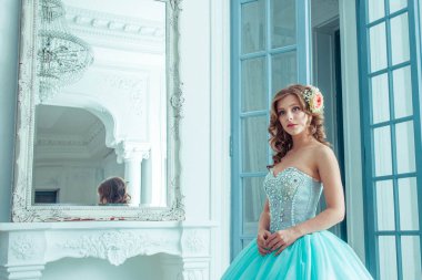 Güzel genç kız uzun, muhteşem turkuaz elbiseli prenses bir ışık kalesinde duruyor. Peri masalı moda fotoğraf çekimi Külkedisi. Güzel oda. Prenses kapıya doğru koşar.