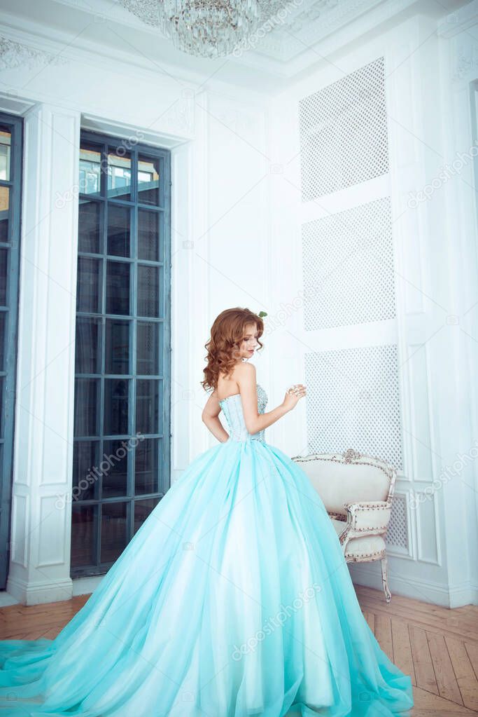 The beautiful young girl the princess in a long magnificent turquoise dress stands in a light castle. Fairytale fashion photo session Cinderella. Beautiful room. 