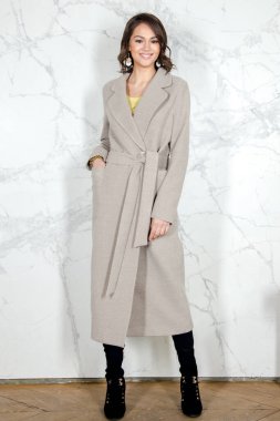 Parlak beyaz bir çatı katı tarzı stüdyosunda açık bej ceketli, kıvırcık saçlı güzellik mankeni kız. Güzel Lüks Kış Kadını. Güzellik ve moda. Bahar ve sonbahar kıyafetleri Stüdyoda poz veren kız