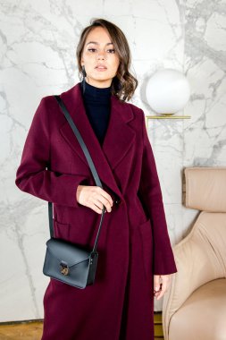 Parlak beyaz çatı katı tarzı stüdyosunda bordo ceketli, kıvırcık saçlı güzellik mankeni kız. Güzel Lüks Kış Kadını. Güzellik ve moda. Bahar ve sonbahar giysileri moda. Stüdyoda poz veren kız.