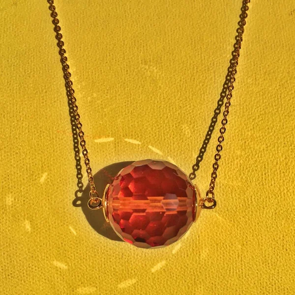 Gold chain with a pendant of sultanite on a yellow background. Sultanite is a stone that changes color under different lighting conditions.